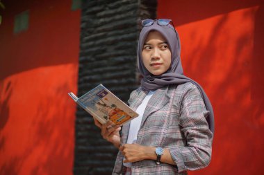 Güzel Asyalı modern tesettür müslüman bayan öğrenci ayakta ve parkta günlüğünü tutuyor.