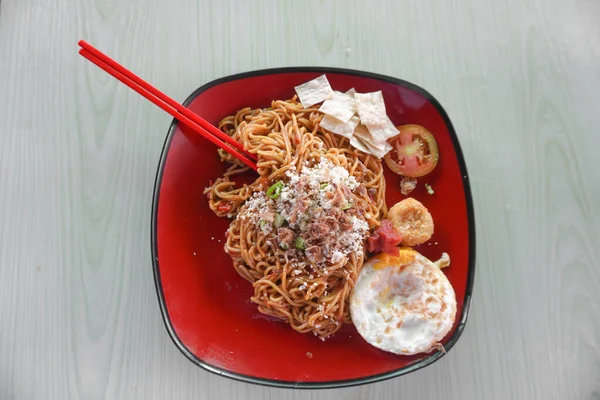 Yumurtalı erişte, naget, domates ve doğranmış tavuk kırmızı tabakta ve ahşap desenli masada lezzetli görünüyor.