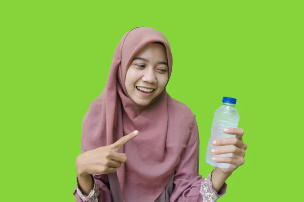 ヒジャーブを身に着けている美しいアジア系イスラム教徒の女性グリーンを背景に手に持っている水のボトルを指しています ムスリム女性ヒジャーブ保持飲料水ボトル用Iftar — ストック写真