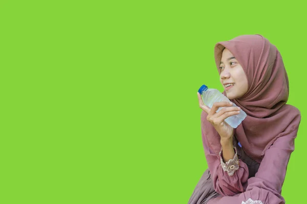 ヒジャーブの笑顔をした美しいアジア系女性緑色の背景で手に水のボトルを持っています イスラム教とラマダーンの概念を持つヒジャーブを着たムスリム女性の写真 — ストック写真