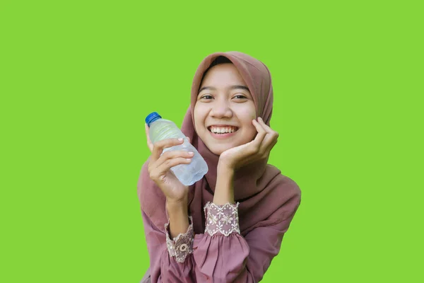 beautiful asian woman wearing hijab smiling and holding water bottle in her hand with green background. photos of Muslim women wearing hijab with Islamic and Ramadan concepts