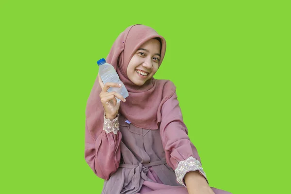 ヒジャーブの笑顔をした美しいアジア系女性緑色の背景で手に水のボトルを持っています イスラム教とラマダーンの概念を持つヒジャーブを着たムスリム女性の写真 — ストック写真