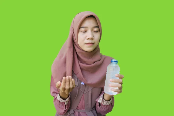 beautiful asian woman wearing hijab holding water bottle and showing prayer gesture for iftar with green background. photos of Muslim women wearing hijab with Islamic and Ramadan concepts