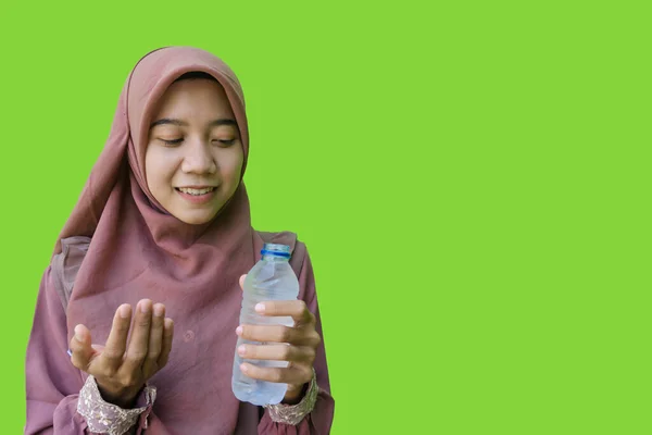 beautiful asian woman wearing hijab holding water bottle and showing prayer gesture for iftar with green background. photos of Muslim women wearing hijab with Islamic and Ramadan concepts