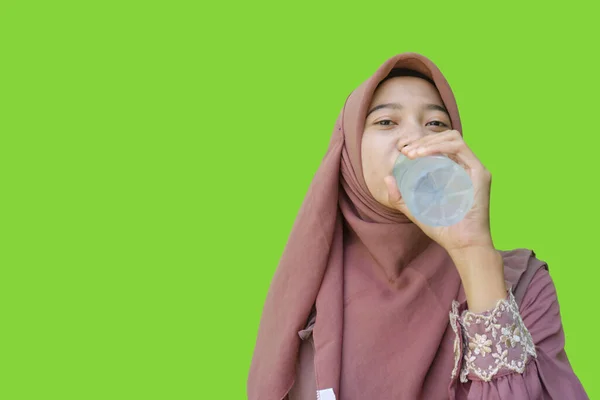 beautiful asian woman wearing hijab breaking fast drinking bottled water with green background. photos of Muslim women wearing hijab with Islamic and Ramadan concepts