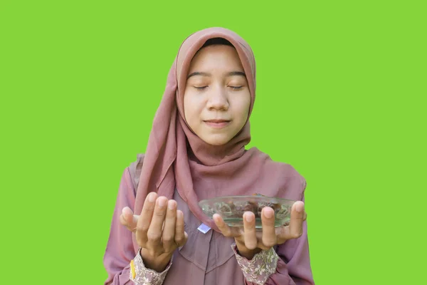 美しいイスラム教徒のアジア人女性ヒジャーブは緑色の背景で断食をしながら日付と祈りのプレートを持っています イスラム教とラマダーンの概念を持つヒジャーブを着たムスリム女性の写真 — ストック写真