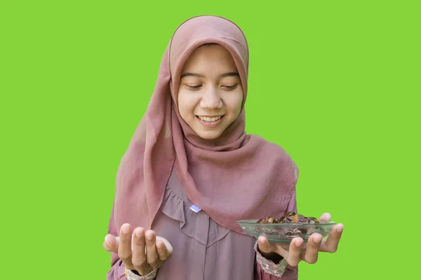 美丽的穆斯林亚洲女人头戴头巾 拿着一盘红枣 一边祈祷一边带着绿色背景快餐店 穆斯林妇女头戴伊斯兰头巾和斋月观念的照片 — 图库照片