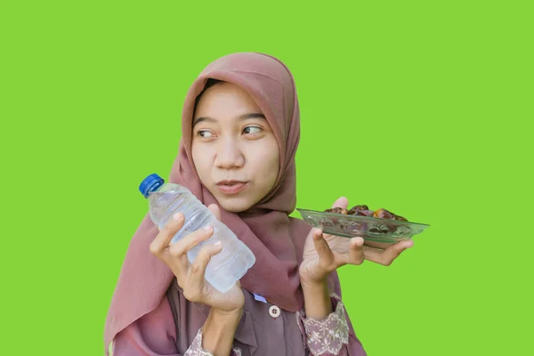 美しいイスラム教徒のアジア人女性ヒジャーブは緑色の背景を持つイフタールのための日付と水のボトルのプレートを保持しています イスラム教とラマダーンの概念を持つヒジャーブを着たムスリム女性の写真 — ストック写真
