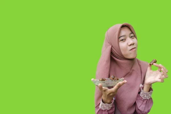 beautiful asian woman hijab eating dates for breaking fast with green background. photo of Muslim women wearing hijab with Islamic and Ramadan concepts