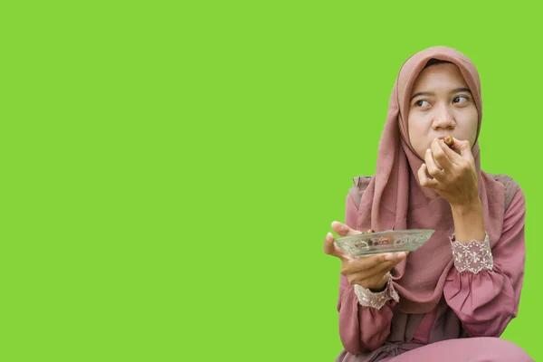美しいアジア系女性のヒジャーブは緑の背景で断食明けのデートを食べています イスラム教とラマダーンの概念を持つヒジャーブを着たムスリム女性の写真 — ストック写真