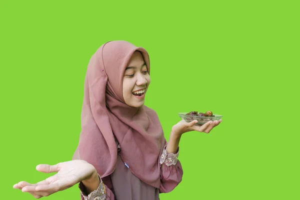 美しいアジア系女性のヒジャーブは緑色の背景で素早く破壊するために日付のプレートを手に持っています イスラム教とラマダーンの概念を持つヒジャーブを着たムスリム女性の写真 — ストック写真