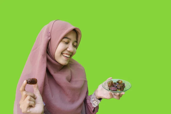美しいアジア系女性のヒジャーブは緑色の背景で素早く破壊するために日付のプレートを手に持っています イスラム教とラマダーンの概念を持つヒジャーブを着たムスリム女性の写真 — ストック写真