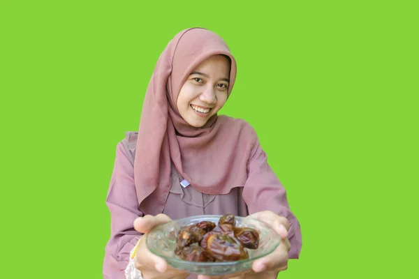 beautiful asian woman hijab holding a plate of dates in her hand for breaking fast with green background. photo of Muslim women wearing hijab with Islamic and Ramadan concepts
