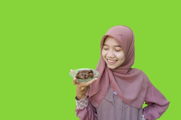 漂亮的亚洲女人戴着头巾 手里拿着一盘红枣 准备带着绿色背景的早餐 穆斯林妇女头戴伊斯兰头巾和斋月观念的照片 — 图库照片