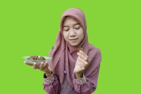 beautiful asian woman hijab holding a plate of dates in her hand for breaking fast with green background. photo of Muslim women wearing hijab with Islamic and Ramadan concepts