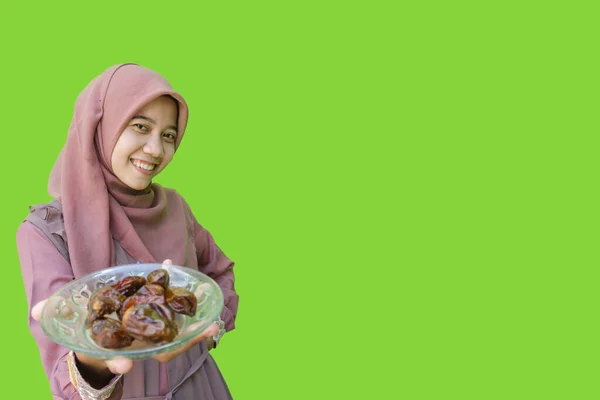 漂亮的亚洲女人戴着头巾 手里拿着一盘红枣 准备带着绿色背景的早餐 穆斯林妇女头戴伊斯兰头巾和斋月观念的照片 — 图库照片