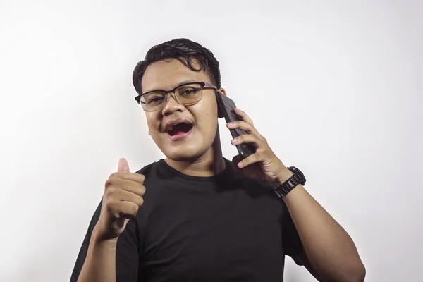 英俊聪明的亚洲年轻人 身穿黑色T恤 打电话给使用智能手机的人 很高兴地表示赞同 大拇指被白色背景隔开 — 图库照片