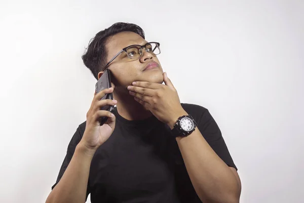 年轻聪明英俊的亚洲男人 身穿黑色T恤 打电话给一个拿着智能手机的人 表达他对白色背景中孤立事物的思考 — 图库照片