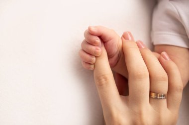 Close-up little hand of child and palm of mother and father. The newborn baby has a firm grip on the parents finger after birth. A newborn holds on to moms, dads finger.