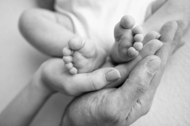 Baby feet in the hands of mother, father, older brother or sister, family. Feet of a tiny newborn close up. Little childrens feet surrounded by the palms of the family. Parents and their child. 