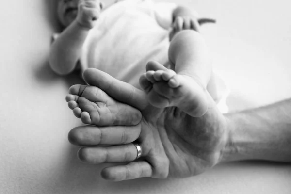 Baby feet in the hands of mother, father, older brother or sister, family. Feet of a tiny newborn close up. Little childrens feet surrounded by the palms of the family. Parents and their child.