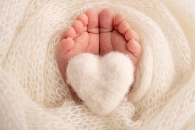 Yeni doğmuş bir bebeğin küçük ayağı. Beyaz yün battaniyenin içinde yeni doğmuş bir bebeğin yumuşak ayakları. Ayak parmakları, topuklar ve yeni doğmuş bir bebeğin ayakları. Bir bebeğin bacaklarında örülmüş beyaz kalp. Makro fotoğrafçılık. 