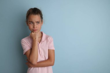 Little emotional teenage girl in pink shirt 11, 12 years old on an isolated blue background. Childrens studio portrait. Place text to copy space for caption, advertising childrens goods. 