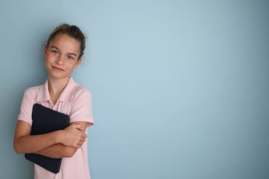 Little emotional teenage girl in pink shirt 11, 12 years old on an isolated blue background with a tablet in her hands.Childrens studio portrait Place the text to copy the place for the inscription