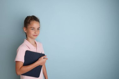 Little emotional teenage girl in pink shirt 11, 12 years old on an isolated blue background with a tablet in her hands.Childrens studio portrait Place the text to copy the place for the inscription