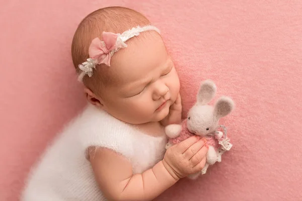 新生児の女の子のトップビューは 白い全体で寝て 彼女の頭の上に白い包帯で ピンクの背景にニットの白いウサギと 新生児の美しい肖像画7日 1週間 — ストック写真