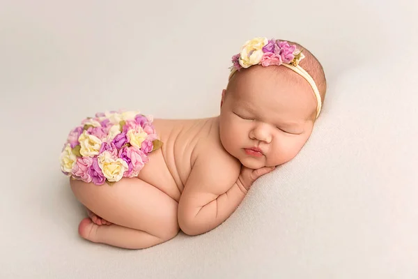 白いフェルトの背景で裸で寝ている新生児のトップビュー 小さな新生児の美しい肖像7日 1週間前白い花のヘッドバンドとカラフルな花を持つ小さな新生児天使 — ストック写真