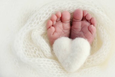 Yeni doğmuş bir bebeğin küçük ayağı. Beyaz yün battaniyenin içinde yeni doğmuş bir bebeğin yumuşak ayakları. Ayak parmakları, topuklar ve yeni doğmuş bir bebeğin ayakları. Bir bebeğin bacaklarında örülmüş beyaz kalp. Makro fotoğrafçılık