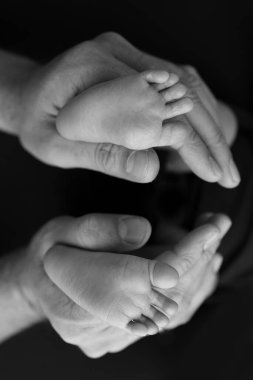 Siyah ve beyaz gölgeli güzel anne elleri, küçük yeni doğmuş bebek ayaklarını sevgi, ilgi, aile güvenliği ve korumayla siyah zemin üzerinde tutun, erken doğum konsepti olan çocuk ya da yoğun bakım