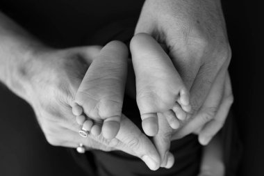 Siyah ve beyaz gölgeli güzel anne elleri, küçük yeni doğmuş bebek ayaklarını sevgi, ilgi, aile güvenliği ve korumayla siyah zemin üzerinde tutun, erken doğum konsepti olan çocuk ya da yoğun bakım