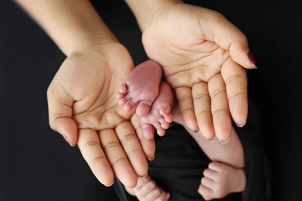 父母的掌心 一位母亲用黑色的毛毯把新生婴儿的脚放在黑色的背景上 新生儿的脚在父母的手里 脚跟和脚趾的照片 — 图库照片
