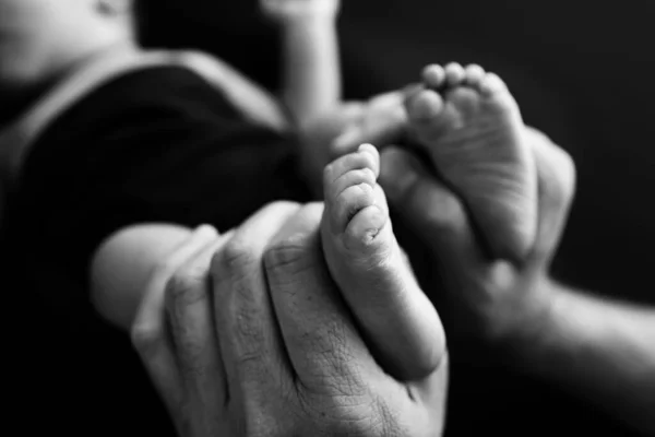 Baby feet in mother hands. Mom and her Child. Happy Family concept. Beautiful conceptual image of Maternity. Black and white photo, black background.