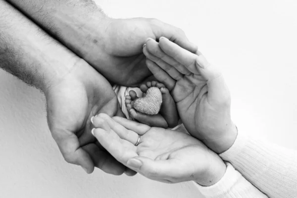 Childrens leg in the hands of mother, father, parents. Feet of a tiny newborn close up. Childrens leg with a knitted heart. Mom her child. Happy family concept. Black and white photo of motherhood.