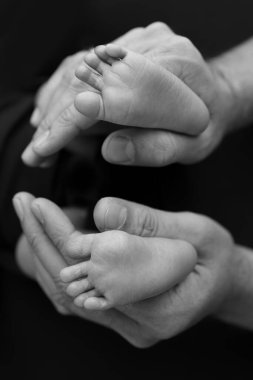 Siyah ve beyaz gölgeli güzel anne elleri, küçük yeni doğmuş bebek ayaklarını sevgi, ilgi, aile güvenliği ve korumayla siyah zemin üzerinde tutun, erken doğum konsepti olan çocuk ya da yoğun bakım