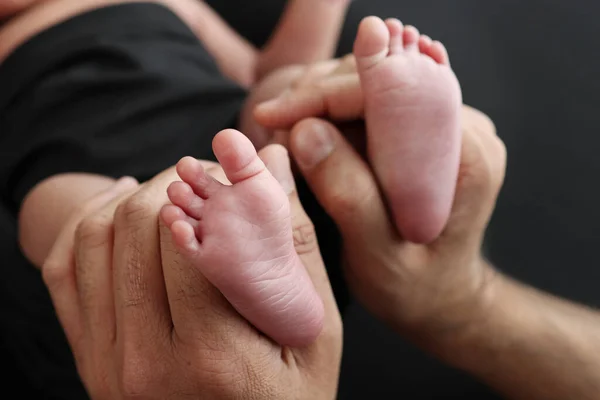一位母亲用黑色的毛毯把新生婴儿的脚放在黑色的背景上 新生儿的脚在父母的手里 新生儿的宏观摄影腿 脚和脚后跟 — 图库照片
