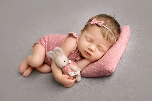 ピンクのスーツを着た可愛い新生児と 頭に蝶が描かれたピンクのヘッドバンドは 甘く眠ります 手に梨のウサギを編んだ 灰色の背景のプロのマクロ写真 — ストック写真