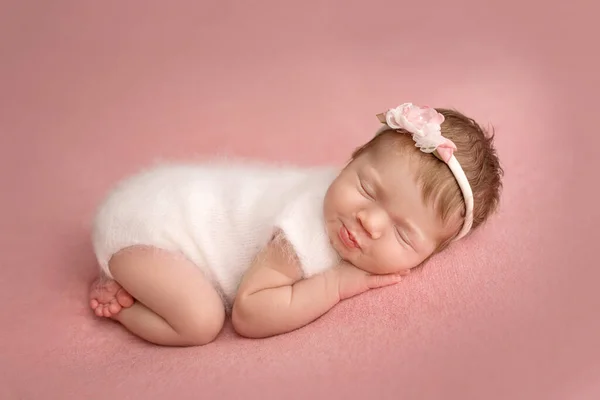 白いジャンプスーツを着た新生児の女の子のトップビュー 彼女の頭の上に花と白い包帯で ピンクの背景に 小さな新生児の美しい肖像画7日 1週間前 — ストック写真