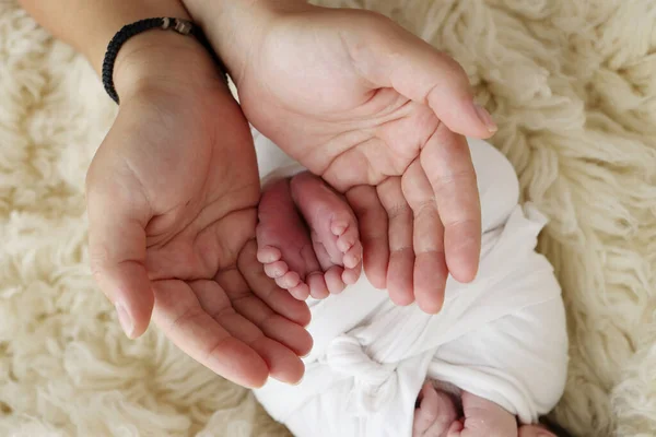 両親の手のひらに新生児の足 父親と母親の手のひらは 新生児の足を白いFlokati毛布で握っています 子供のつま先 かかとと足の写真 — ストック写真