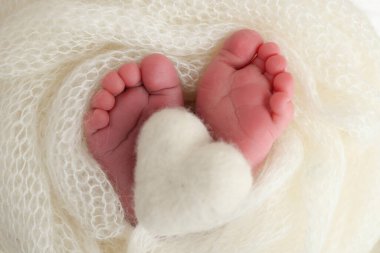 Yeni doğmuş bir bebeğin küçük ayağı. Beyaz yün battaniyenin içinde yeni doğmuş bir bebeğin yumuşak ayakları. Ayak parmakları, topuklar ve yeni doğmuş bir bebeğin ayakları. Bir bebeğin bacaklarında örülmüş beyaz kalp. Makro fotoğrafçılık