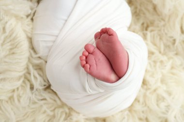 Yeni doğmuş bir bebeğin küçük ayağı. Beyaz arka planda beyaz yün bir flaccati içinde yumuşak bir bebeğin ayakları. Ayak parmaklarının, topuklarının ve ayaklarının makro fotoğrafı.. 