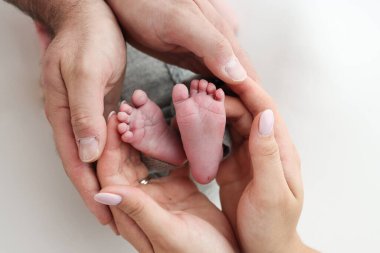 Annenin, babanın avuç içleri yeni doğan bebeğin ayağını beyaz arka planda tutuyor. Yeni doğan bebeğin ayakları, ebeveynlerin avuçlarında. Bir çocuğun ayak parmaklarının, topuklarının ve ayaklarının fotoğrafı