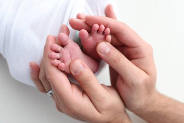Annenin, babanın avuç içleri yeni doğan bebeğin ayağını beyaz arka planda tutuyor. Yeni doğan bebeğin ayakları, ebeveynlerin avuçlarında. Bir çocuğun ayak parmaklarının, topuklarının ve ayaklarının fotoğrafı