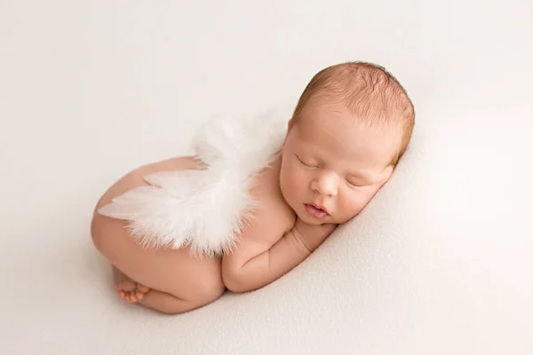 A cute newborn boy in the first days of life sleeps naked on a white fabric background. New born baby with angel white wings. High quality photo.