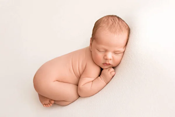 A cute newborn boy in the first days of life sleeps naked on a white fabric background. New born baby with angel white wings. High quality photo.