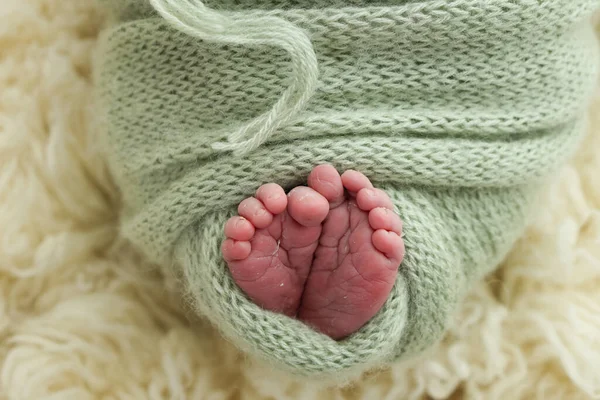Yeni doğmuş bir bebeğin küçük ayağı. Yeşil, şam fıstıklı, beyaz bir flaccati arka planda zeytinli battaniyeli bir bebeğin yumuşak ayakları. Ayak parmaklarının, topuklarının ve ayaklarının makro fotoğrafı.. 