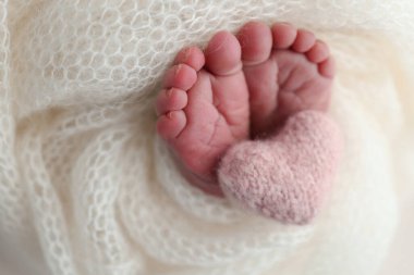 Yeni doğmuş bir bebeğin küçük ayağı. Beyaz yün battaniyenin içinde yeni doğmuş bir bebeğin yumuşak ayakları. Ayak parmakları, topuklar ve yeni doğmuş bir bebeğin ayakları. Bir bebeğin bacaklarında pembe bir kalp örülmüş. Makro fotoğrafçılık 